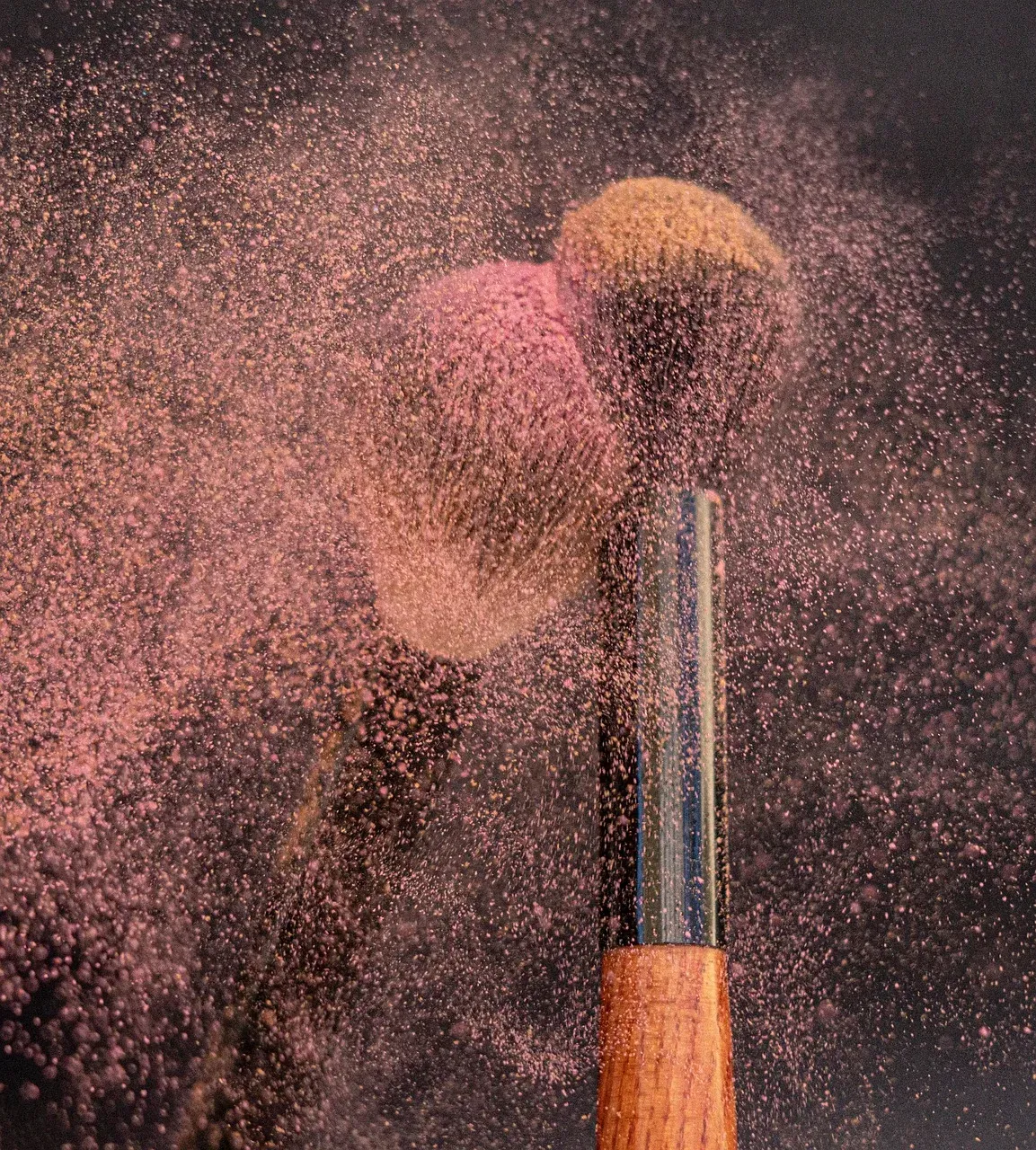 A blush brush in a cloud of pink powder.