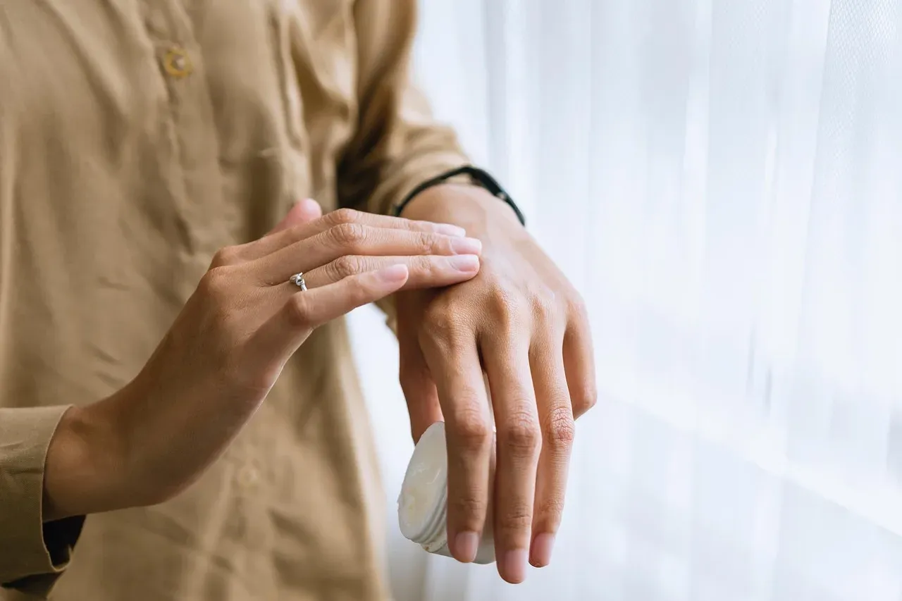A woman applying cream to the back of her hand.