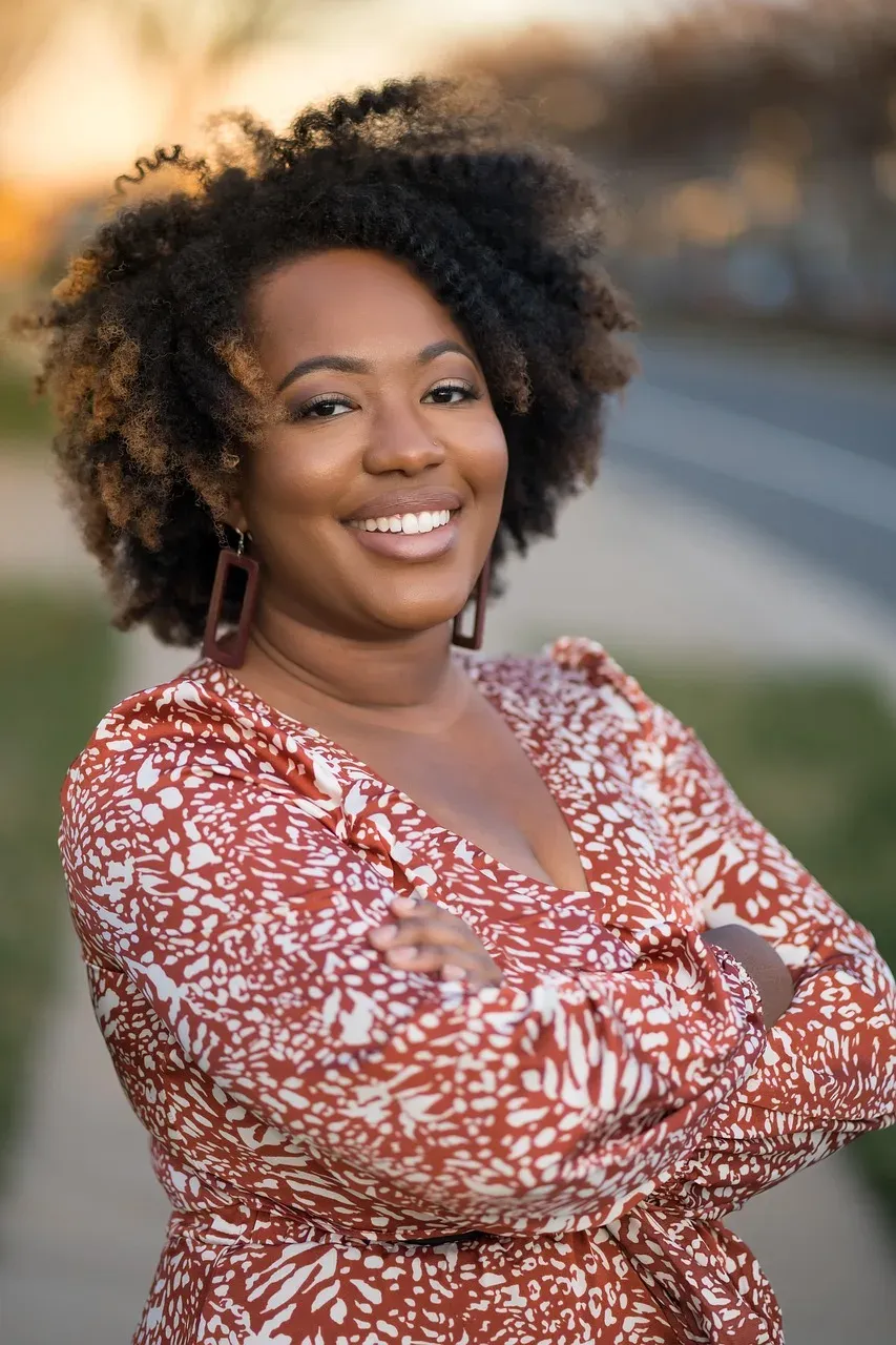 A smiling woman with full curly hair in a red patterned blouse.