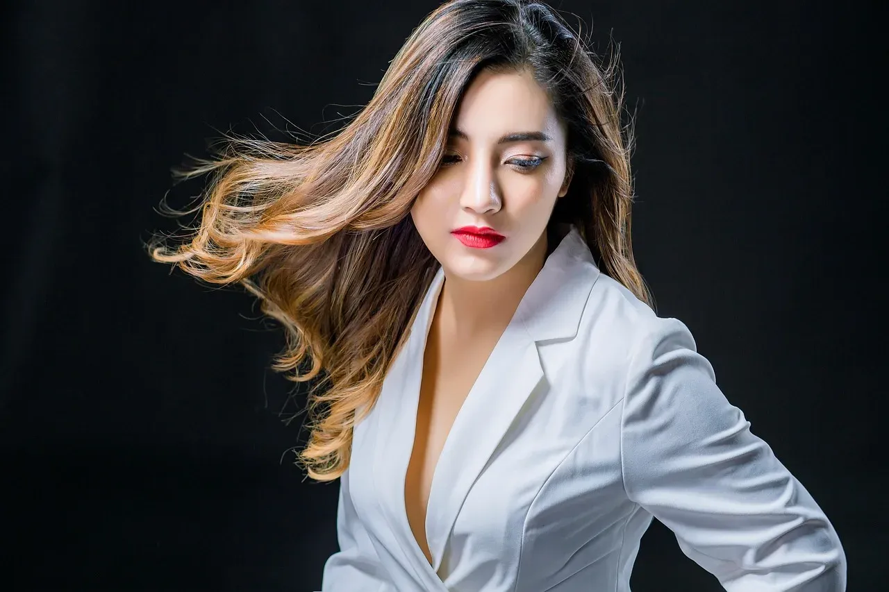 A woman in a white suit and red lipstick, her hair in motion.